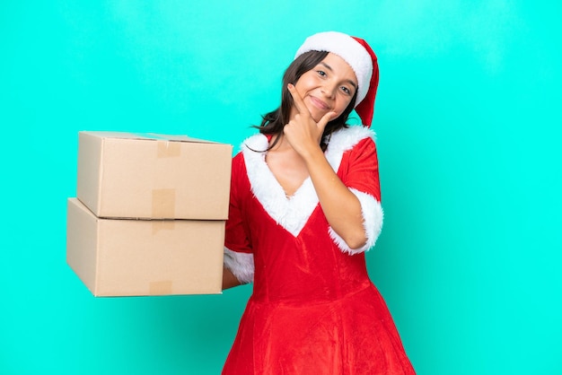 Young hispanic woman dressed as mama noel holding cartoon box\
isolated on blue background happy and smiling