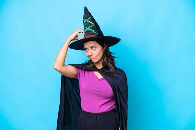 Young hispanic woman dressed as witch over isolated background having doubts while scratching head