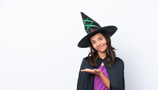 Young hispanic woman dressed as witch over isolated background presenting an idea while looking smiling towards