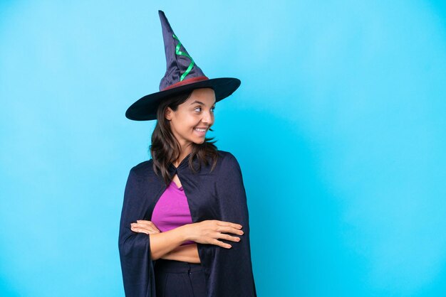 Young hispanic woman dressed as witch over isolated background with arms crossed and happy