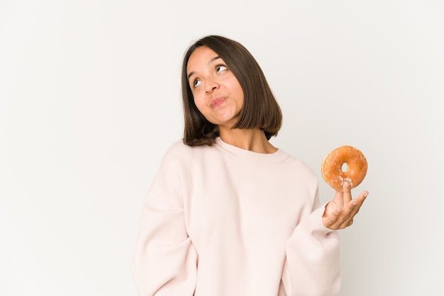 Young hispanic woman eating a doughnut dreaming of achieving goals and purposes