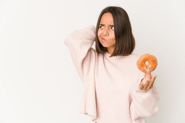 Young hispanic woman eating a doughnut touching back of head