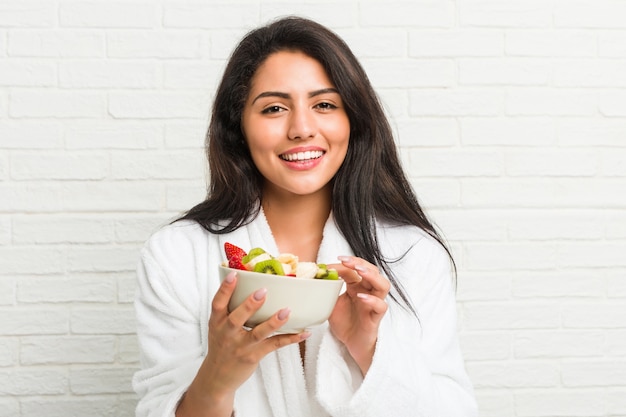 Young hispanic woman eating a fruit bowl on the bed