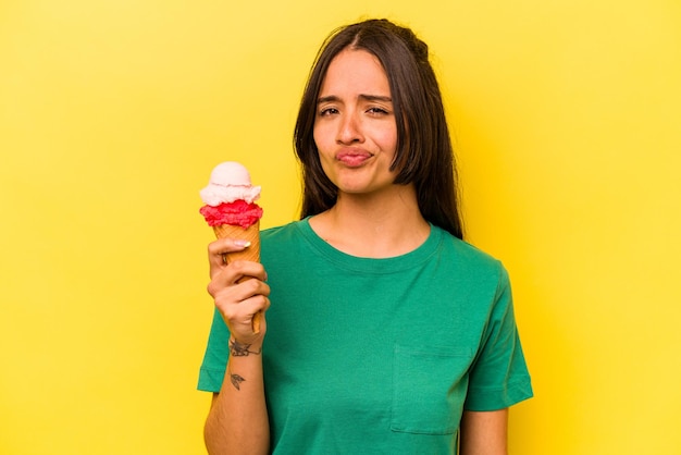 노란색 배경에 격리된 아이스크림을 먹는 젊은 히스패닉 여성