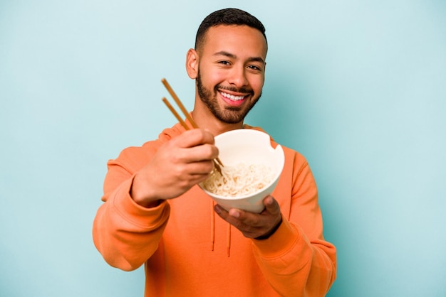 Young hispanic woman eating noodles isolated on blue background