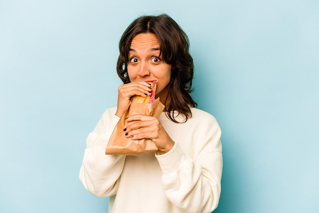 Young hispanic woman eating a sandwich isolates on blue background