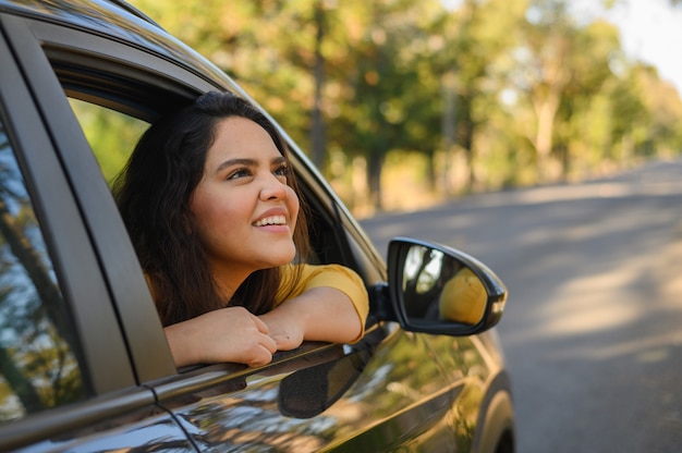 Young Hispanic woman enjoying sun out of car window on a bright day