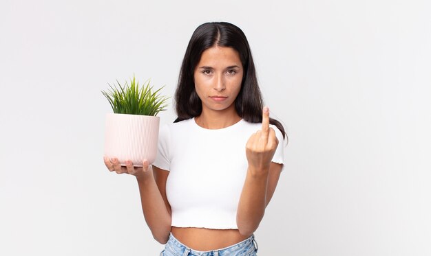 Young hispanic woman feeling angry, annoyed, rebellious and aggressive and holding a decorative house plant