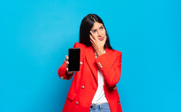 Young hispanic woman feeling bored, frustrated and sleepy after a tiresome, dull and tedious task, holding face with hand. phone screen copy space