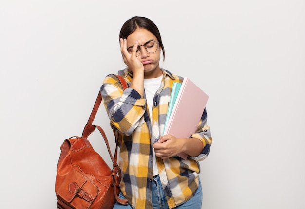 Young hispanic woman feeling bored, frustrated and sleepy after a tiresome, dull and tedious task, holding face with hand