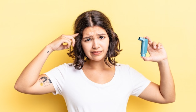 Young hispanic woman feeling confused and puzzled, showing you are insane. asthma concept