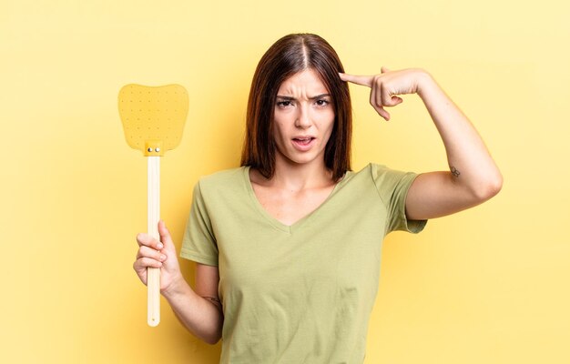 Young hispanic woman feeling confused and puzzled showing you are insane kill flies concept