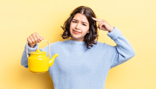 Young hispanic woman feeling confused and puzzled, showing you are insane. teapot concept