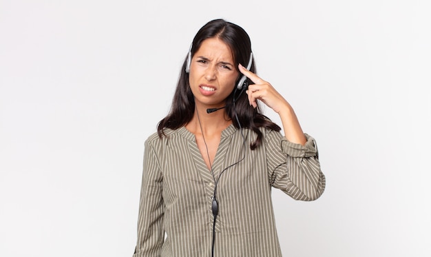 Young hispanic woman feeling confused and puzzled, showing you are insane with a headset. telemarketing concept