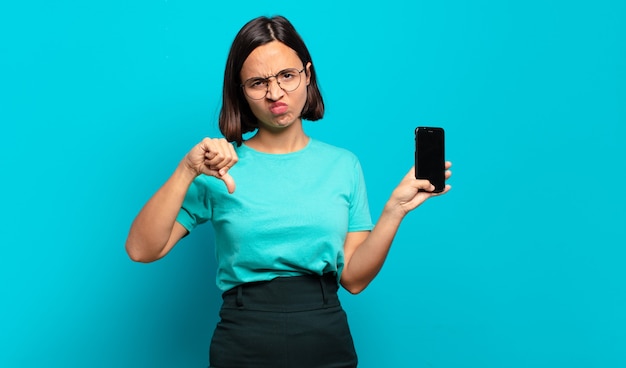 Young hispanic woman feeling cross, angry, annoyed, disappointed or displeased, showing thumbs down with a serious look