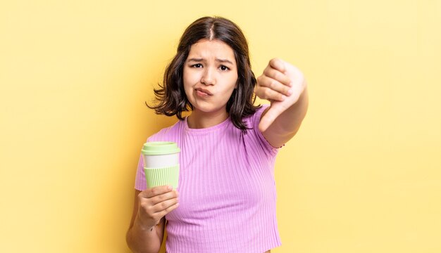 young hispanic woman feeling cross,showing thumbs down. take away coffee concept