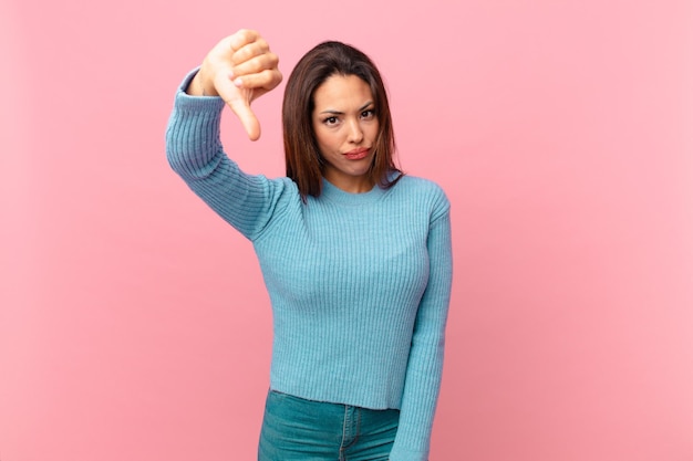 young hispanic woman feeling cross,showing thumbs down