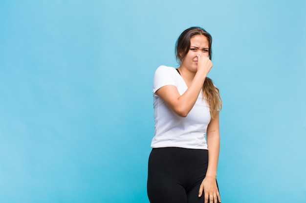 Young hispanic woman feeling disgusted, holding nose to avoid smelling a foul and unpleasant stench