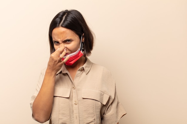 嫌悪感を感じ、悪臭や不快な悪臭を避けるために鼻を抱えている若いヒスパニック系女性