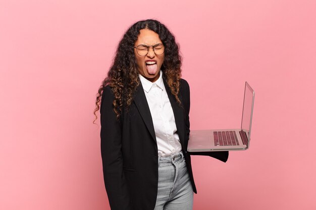 Young hispanic woman feeling disgusted and irritated, sticking tongue out, disliking something nasty and yucky