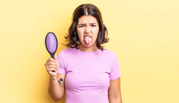 Young hispanic woman feeling disgusted and irritated and tongue out. hairbrush concept