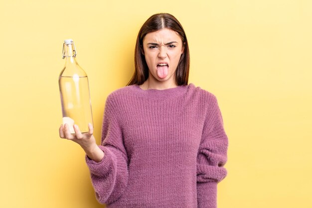 Giovane donna ispanica che si sente disgustata e irritata e con la lingua fuori. concetto di bottiglia d'acqua