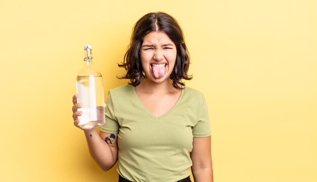 Foto giovane donna ispanica che si sente disgustata e irritata e con la lingua fuori il concetto di bottiglia d'acqua