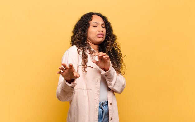 Young hispanic woman feeling disgusted and nauseous, backing away from something nasty, smelly or stinky, saying yuck