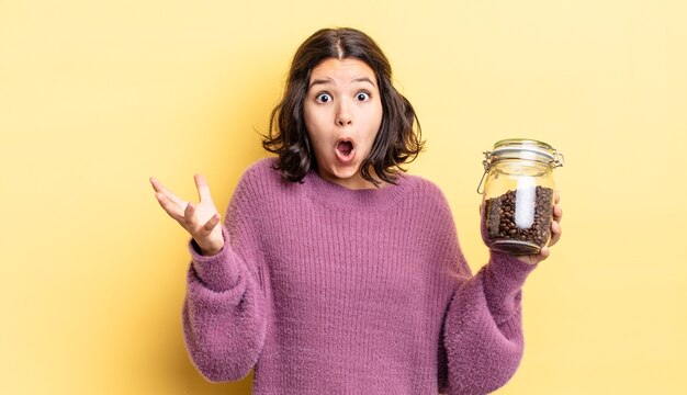 young hispanic woman feeling extremely shocked and surprised. coffee beans concept