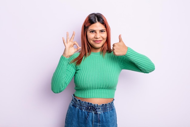 Young hispanic woman feeling happy, amazed, satisfied and surprised, showing okay and thumbs up gestures, smiling