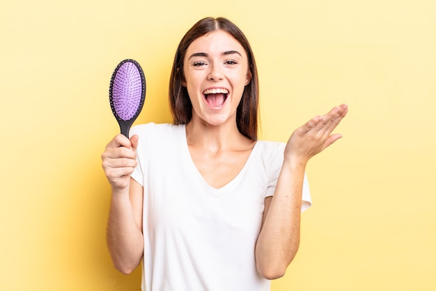 Young hispanic woman feeling happy and astonished at something unbelievable. hair brush concept