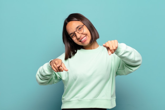 Young hispanic woman feeling happy and confident, pointing to front with both hands and laughing, choosing you