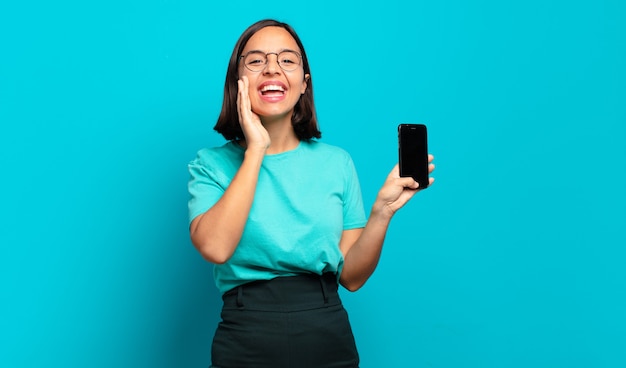 Young hispanic woman feeling happy, excited and positive, giving a big shout out with hands next to mouth