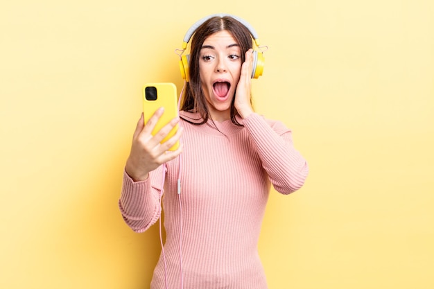 Young hispanic woman feeling happy, excited and surprised. headphones and telephone concept