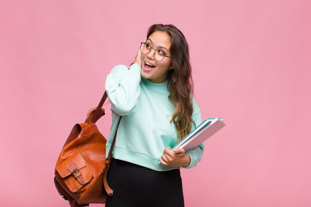 Young hispanic woman feeling happy, excited and surprised, looking to the side with both hands on face