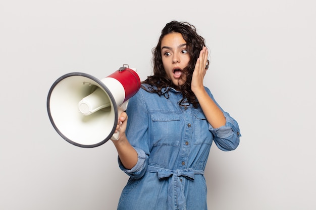 Young hispanic woman feeling happy, excited and surprised, looking to the side with both hands on face