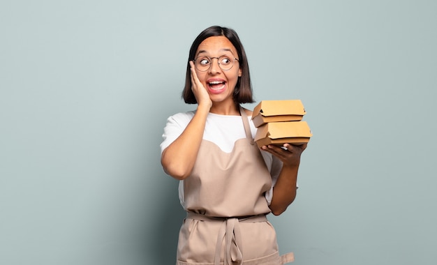 Young hispanic woman feeling happy, excited and surprised, looking to the side with both hands on face