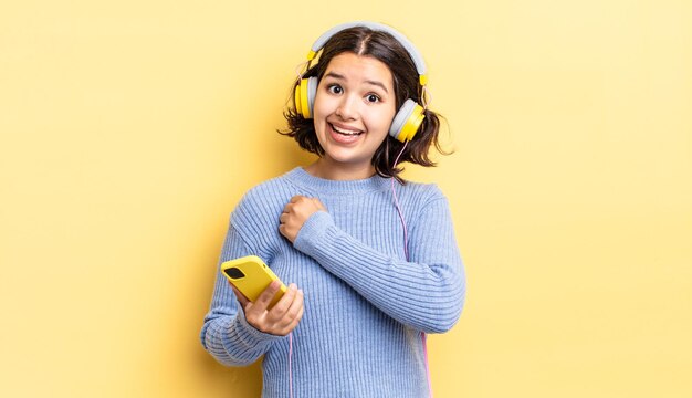 Young hispanic woman feeling happy and facing a challenge or celebrating. headphones and smartphone concept