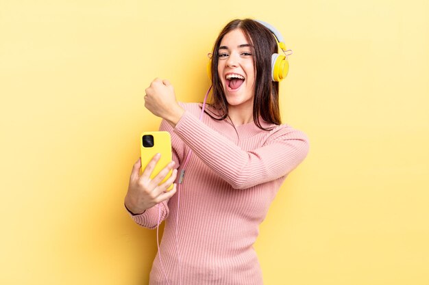 Young hispanic woman feeling happy and facing a challenge or celebrating. headphones and telephone concept