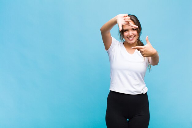 Young hispanic woman feeling happy, friendly and positive, smiling and making a portrait or photo frame with hands