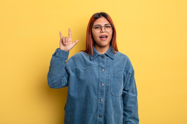 Foto giovane donna ispanica che si sente felice, divertente, sicura di sé, positiva e ribelle, facendo segno rock o heavy metal con la mano