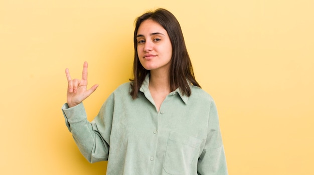 Foto giovane donna ispanica che si sente felice, divertente, fiducioso, positivo e ribelle che fa segno rock o heavy metal con la mano