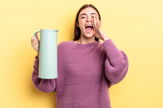 young hispanic woman feeling happy,giving a big shout out with hands next to mouth. coffee thermos concept