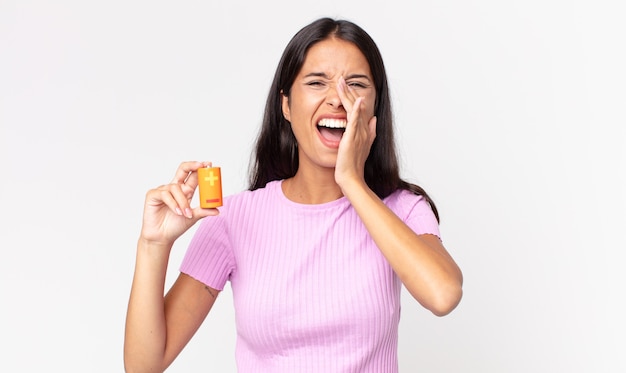 Young hispanic woman feeling happy,giving a big shout out with hands next to mouth and holding batteries