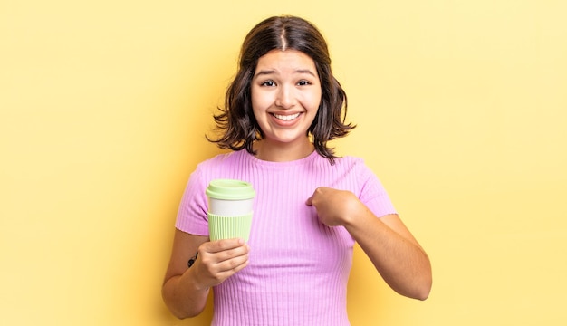 Молодая латиноамериканская женщина чувствует себя счастливой и с возбуждением указывает на себя. концепция кофе на вынос