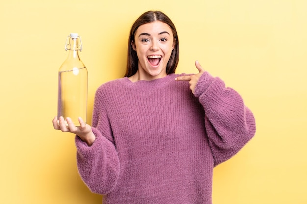 Young hispanic woman feeling happy and pointing to self with an excited. water bottle concept