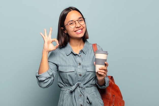 Young hispanic woman feeling happy, relaxed and satisfied, showing approval with okay gesture, smiling