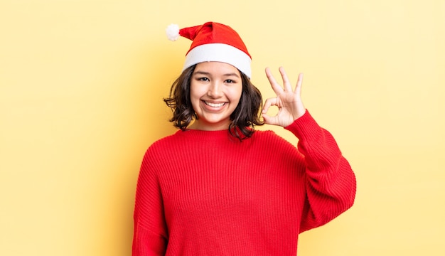 Молодая латиноамериканская женщина чувствует себя счастливой, показывая одобрение жестом в порядке. рождественская концепция