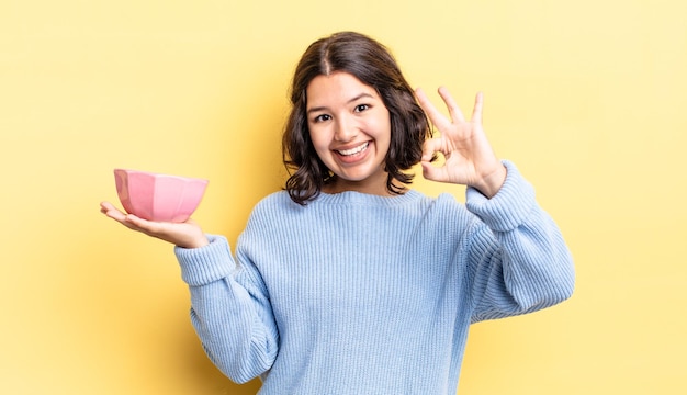 Young hispanic woman feeling happy, showing approval with okay gesture. empty bowl concept