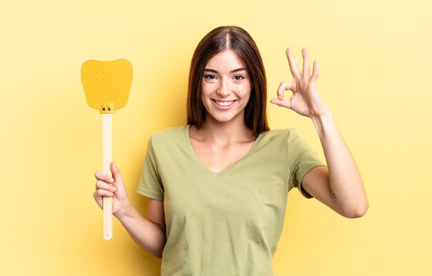 young hispanic woman feeling happy, showing approval with okay gesture. kill flies concept